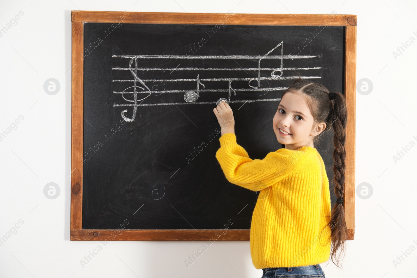 Photo of Little girl writing music notes on blackboard in classroom