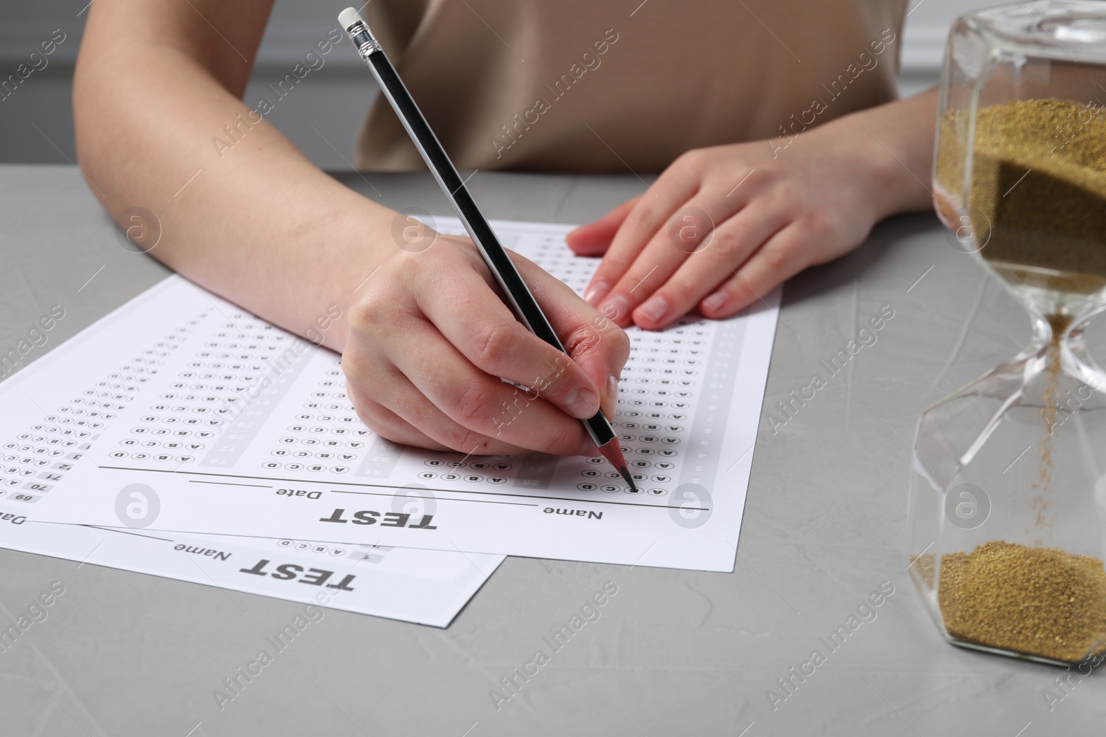 Photo of Student filling answer sheet at light grey table, closeup. Passing exam