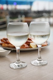 Photo of Glasses of white wine and delicious cooked shrimps served on wooden table outdoors