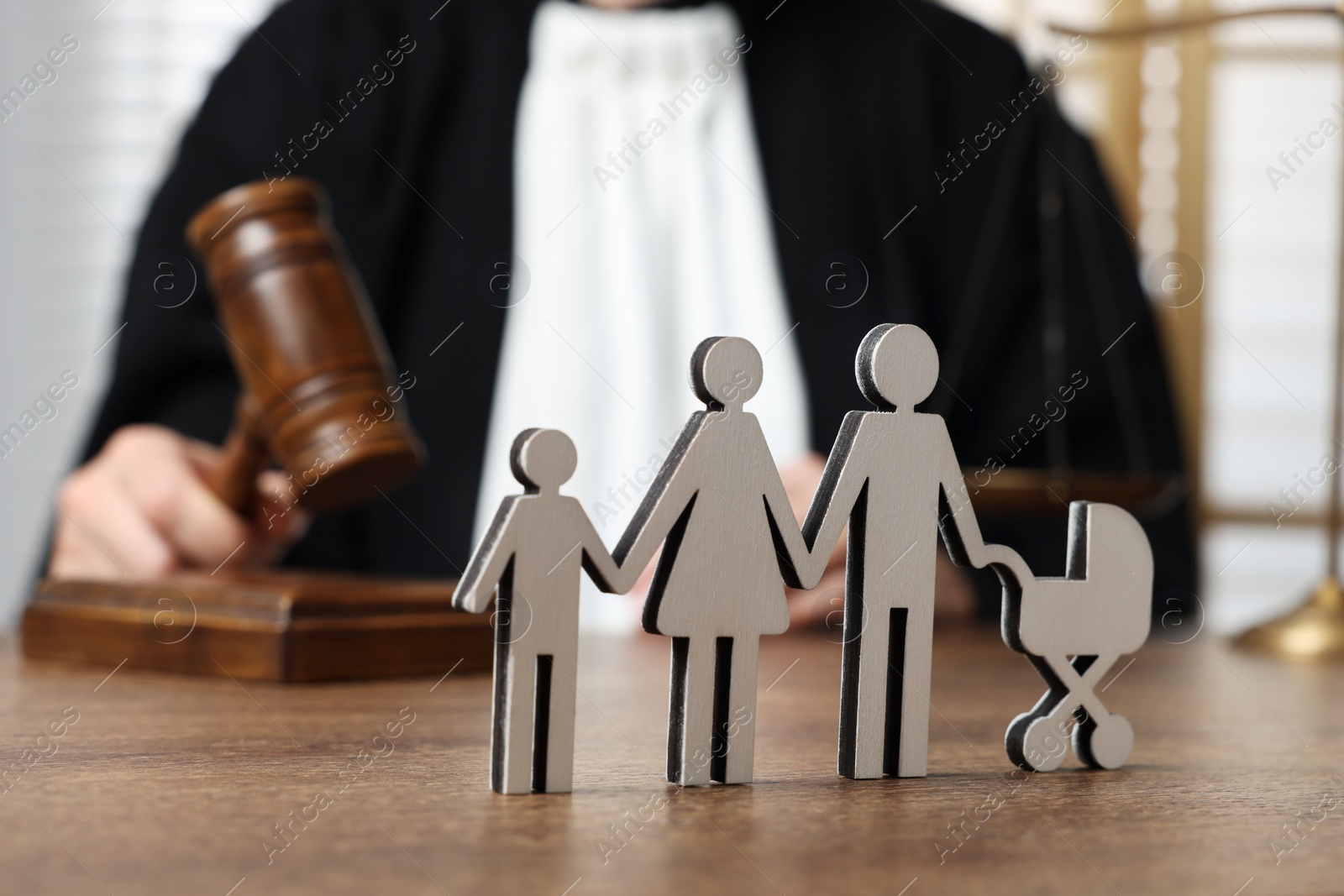 Photo of Family law. Judge with gavel sitting at wooden table, focus on figure of parents and children