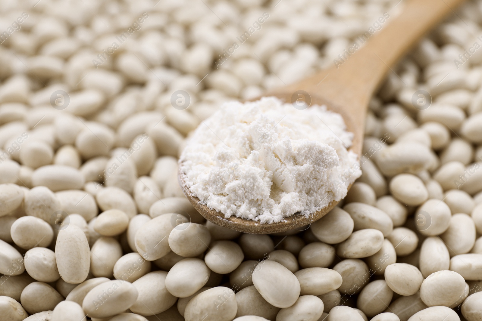 Photo of Wooden spoon with flour on white kidney beans, closeup. Space for text