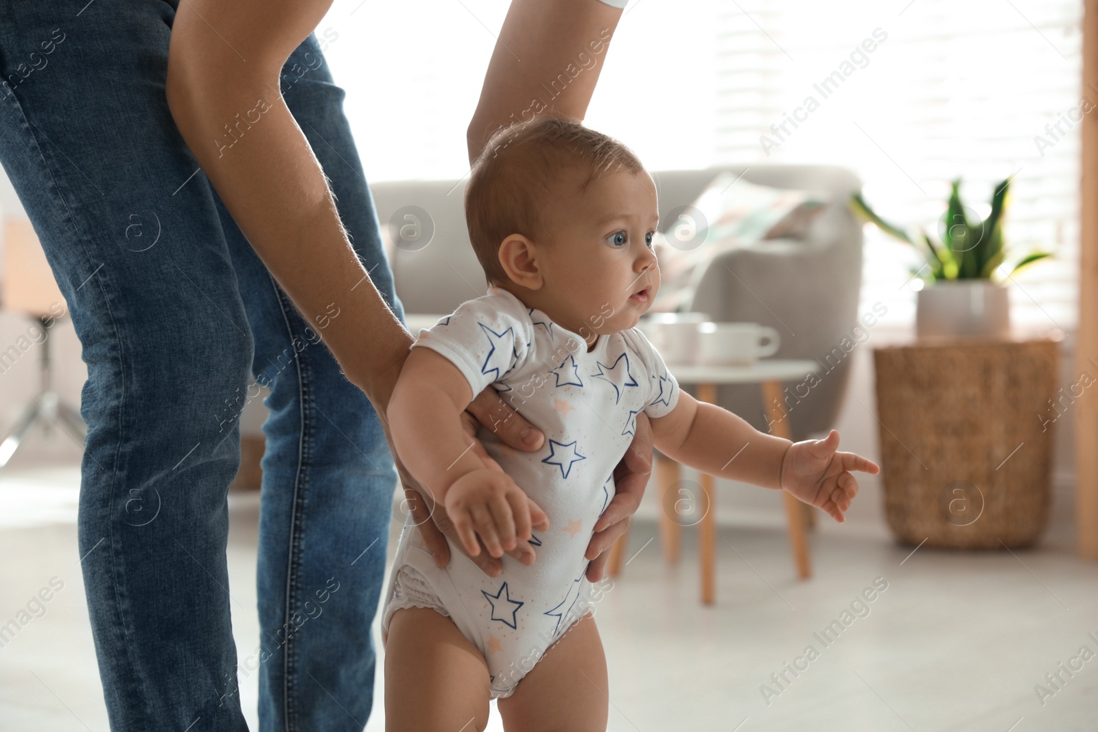 Photo of Father supporting his baby daughter while she learning to walk at home