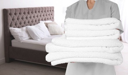Chambermaid with clean folded towels near bed in hotel room, closeup