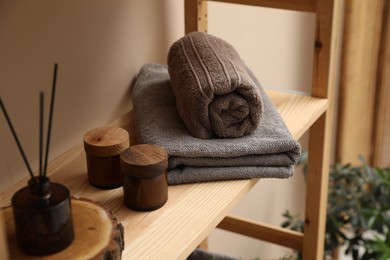 Photo of Soft towels, candles and air freshener on wooden shelf indoors, closeup