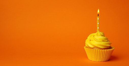 Delicious birthday cupcake with yellow cream and burning candle on orange background. Space for text