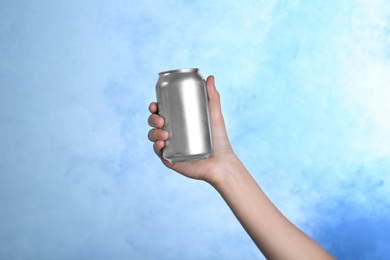 Woman holding aluminum can with beverage on color background