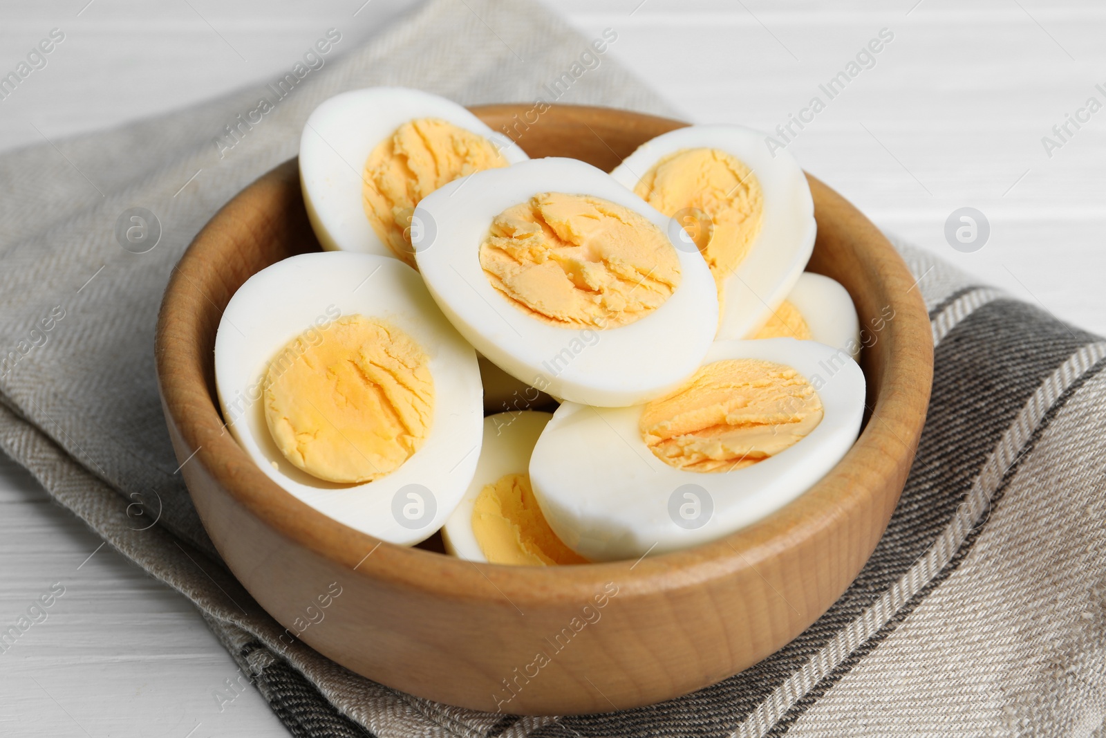 Photo of Cut hard boiled chicken eggs in wooden bowl on table