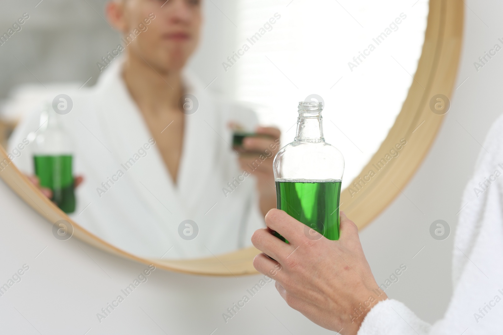 Photo of Young man using mouthwash near mirror in bathroom, closeup