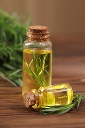 Bottles of essential oil and fresh tarragon leaves on wooden table