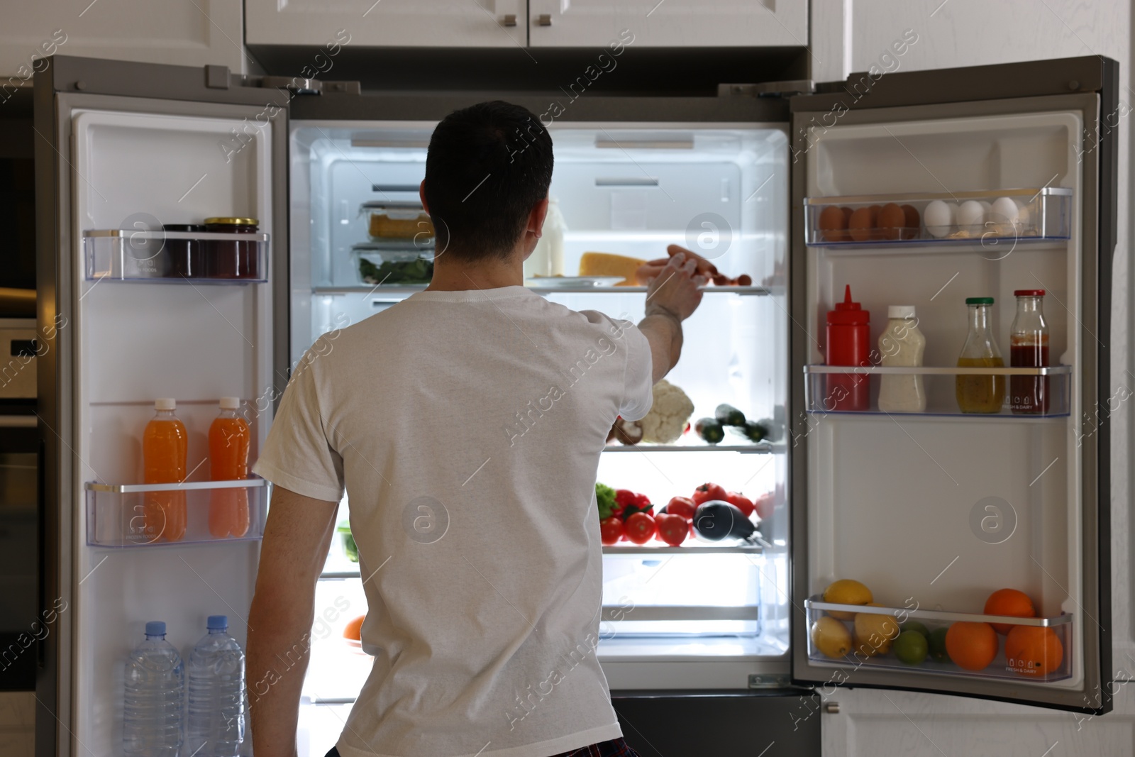 Photo of Man near refrigerator in kitchen, back view