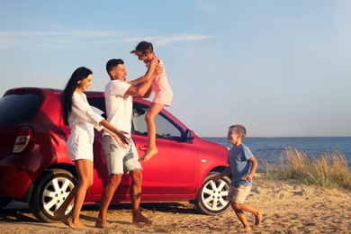 Photo of Happy family having fun near car on sandy beach. Summer trip