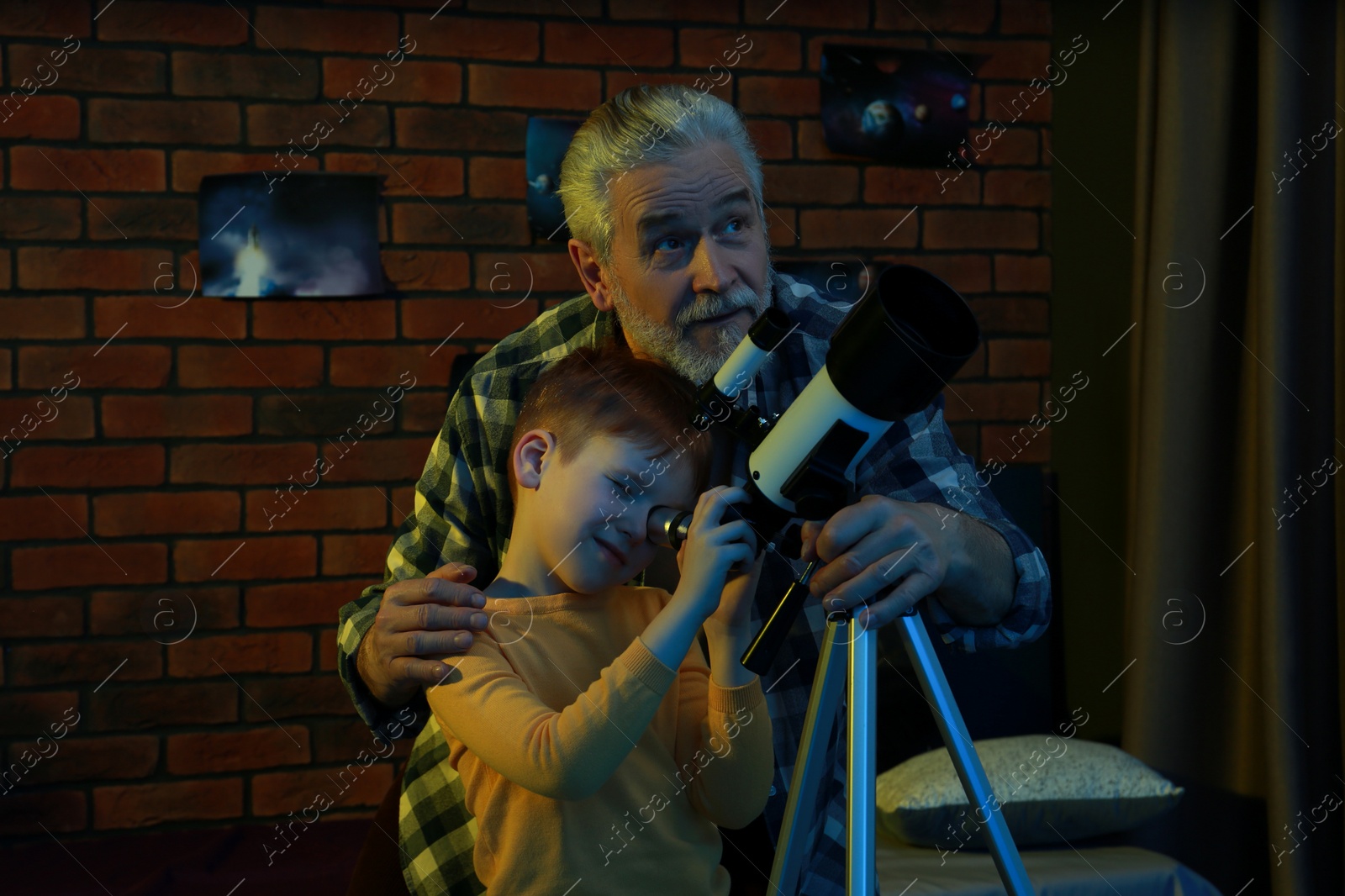 Photo of Little boy with his grandfather looking at stars through telescope in room