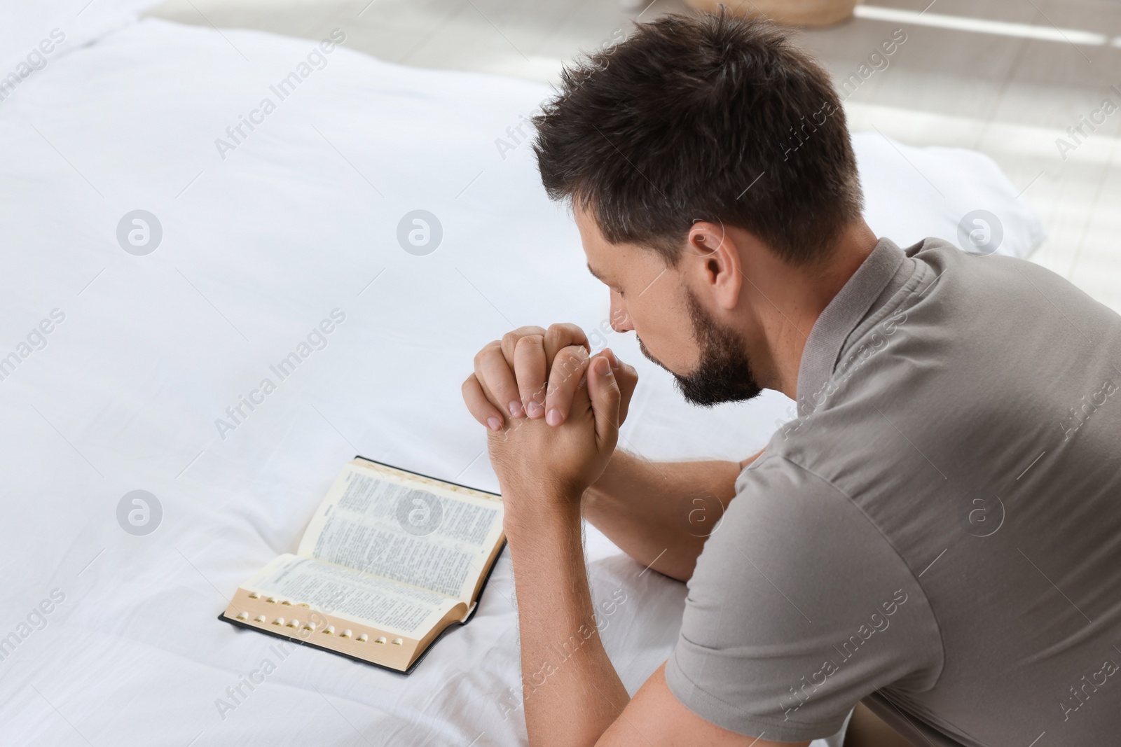 Photo of Religious man with Bible praying in bedroom