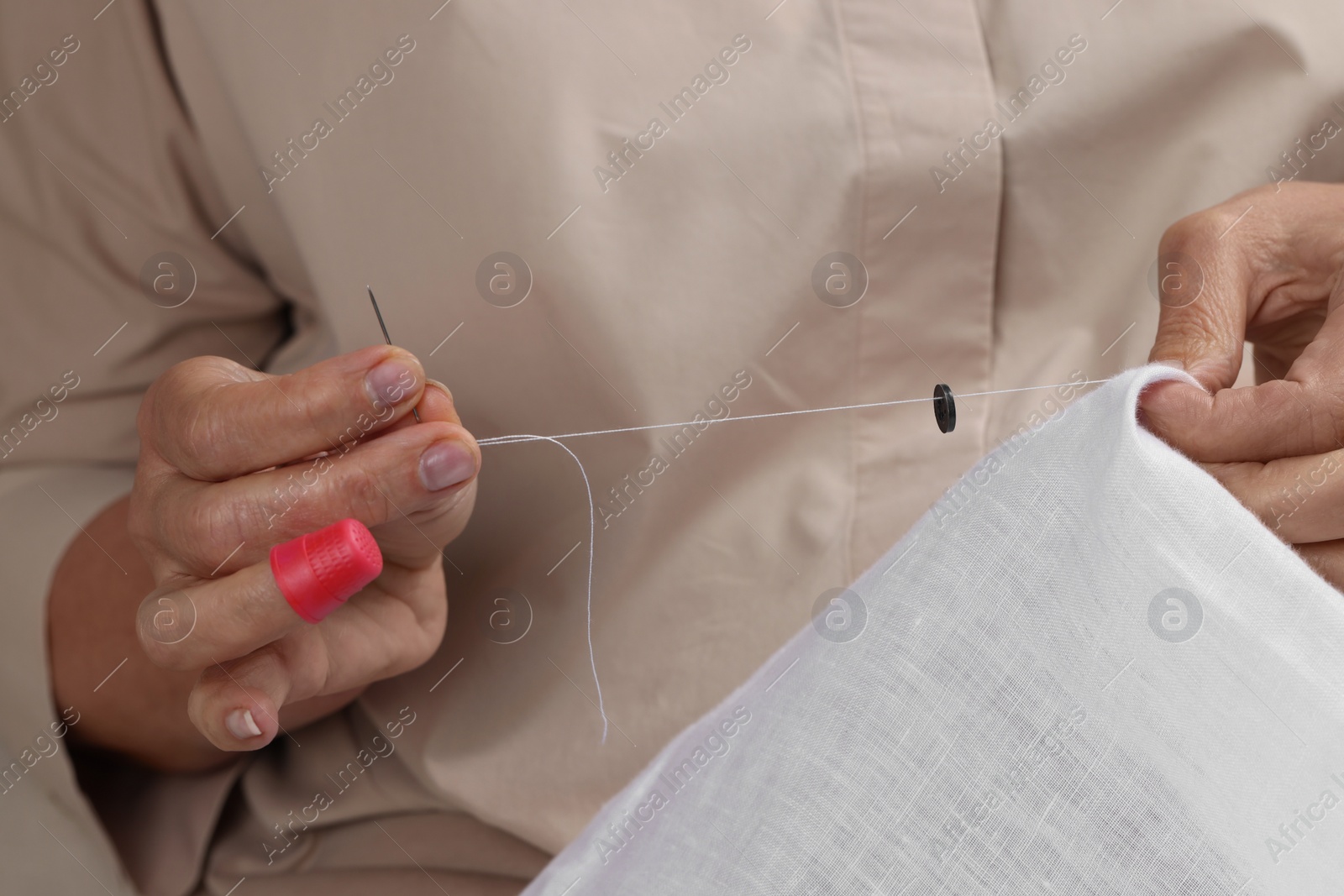 Photo of Woman sewing button with thimble and needle, closeup