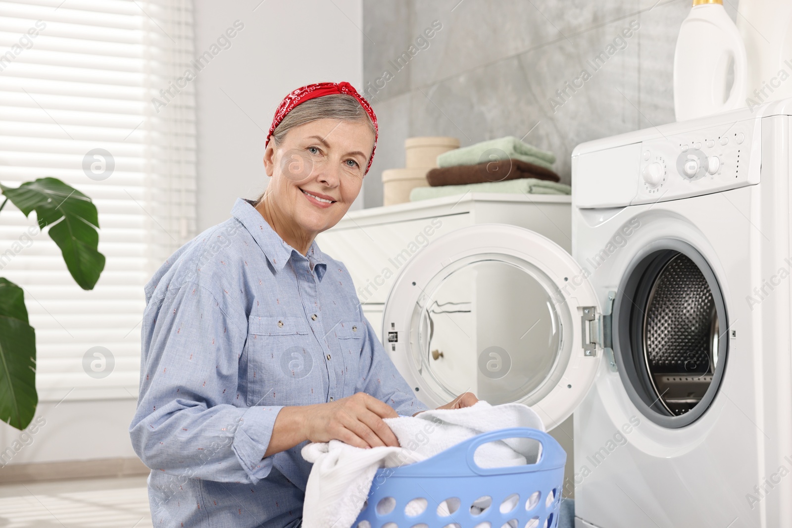 Photo of Happy housewife with laundry basket near washing machine at home