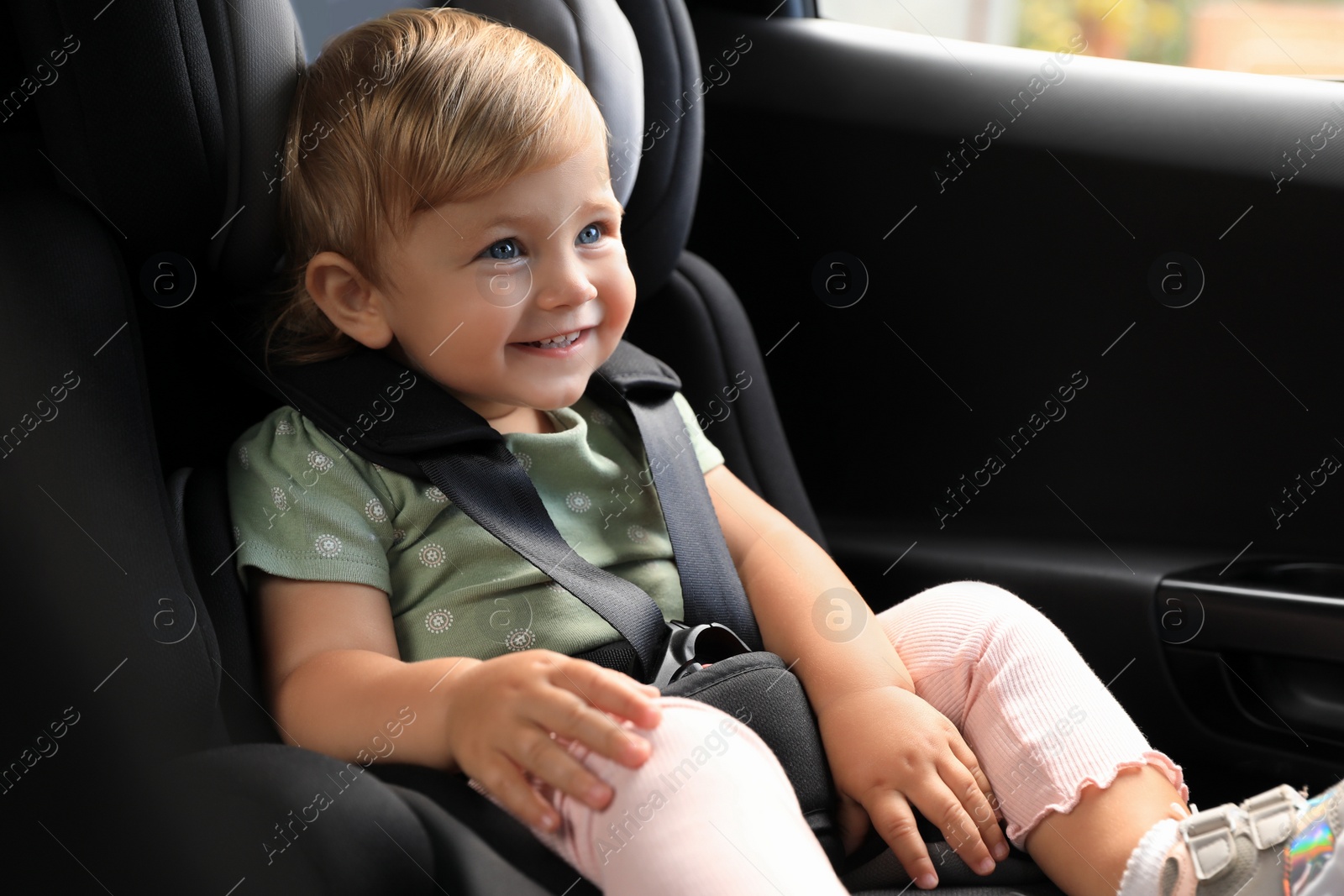 Photo of Cute little girl sitting in child safety seat inside car