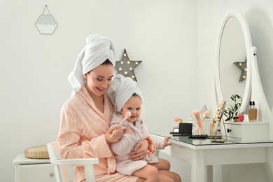 Photo of Young mother and little daughter doing makeup at dressing table