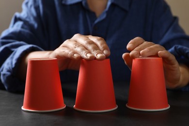 Woman playing thimblerig game with red cups at black table, closeup