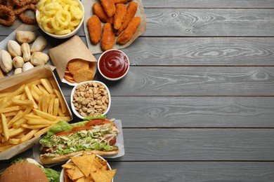 Photo of French fries, onion rings and other fast food on gray wooden table, flat lay with space for text