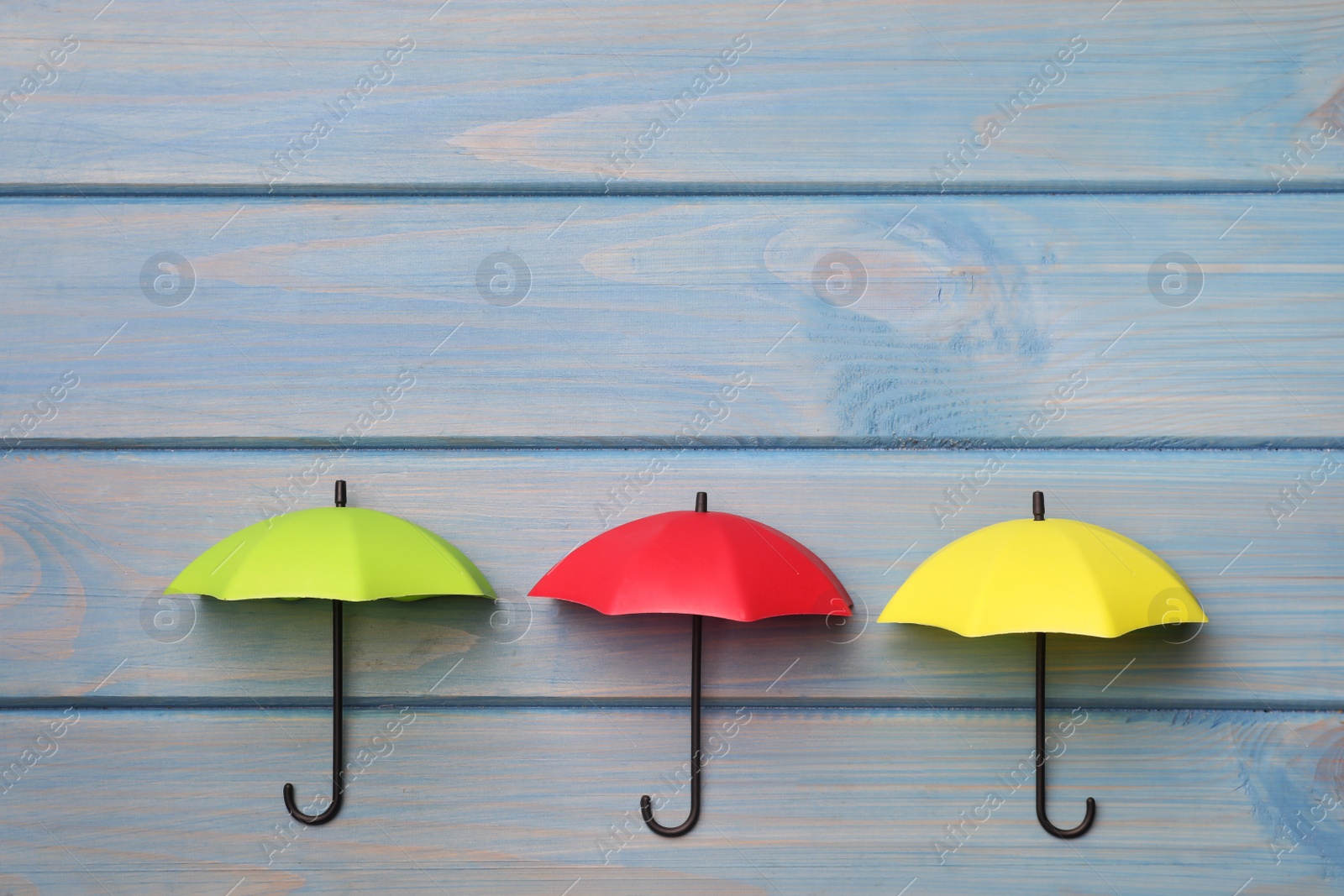 Photo of Small color umbrellas on light blue wooden background, flat lay. Space for text