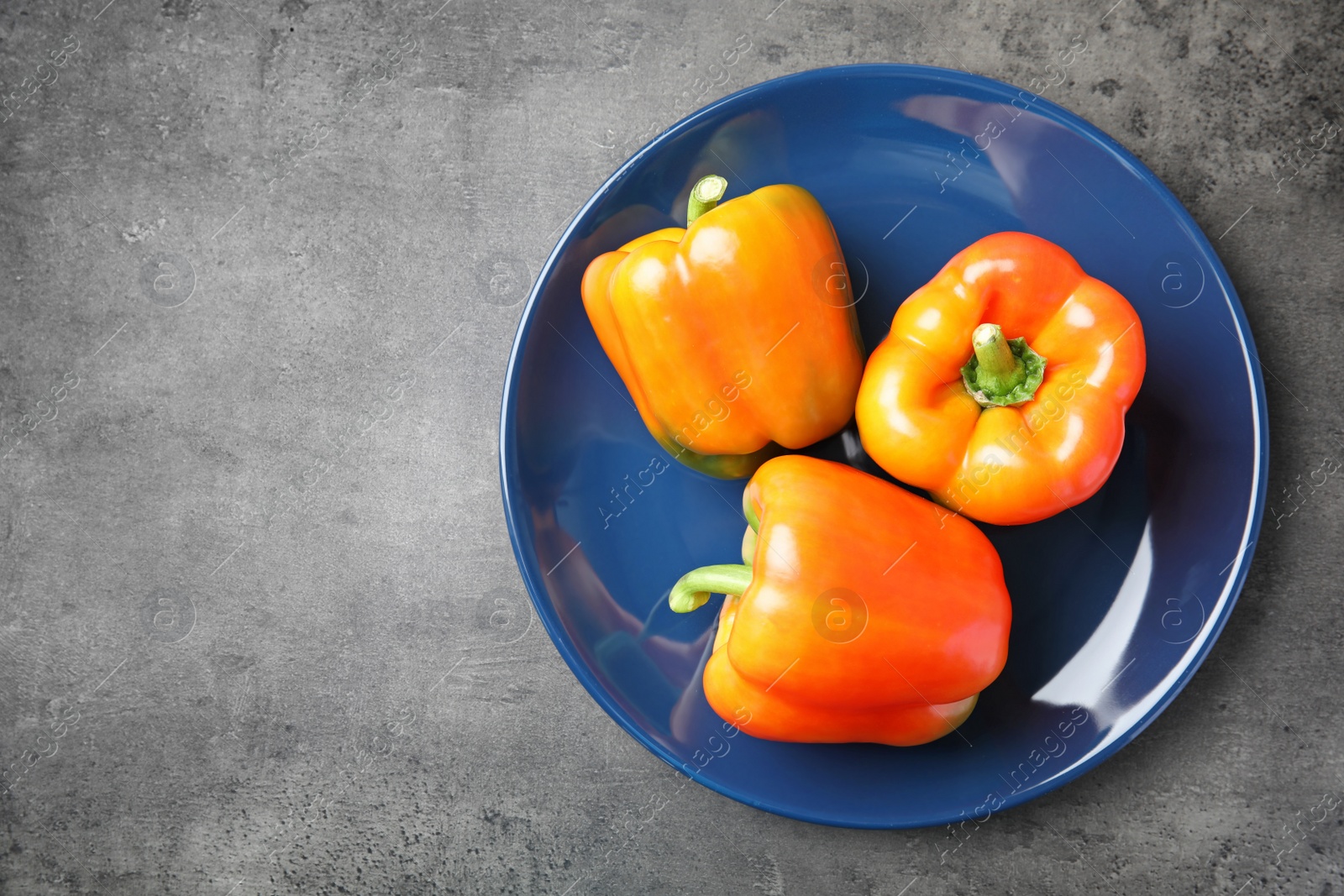 Photo of Plate with ripe paprika peppers on grey background, top view