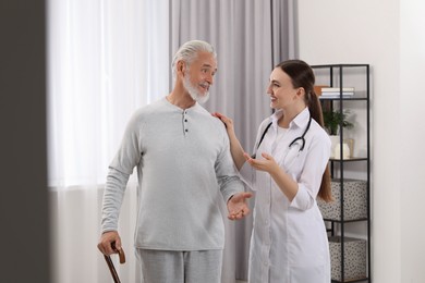 Photo of Young healthcare worker assisting senior man with walking cane indoors