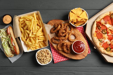 French fries, onion rings and other fast food on gray wooden table, flat lay