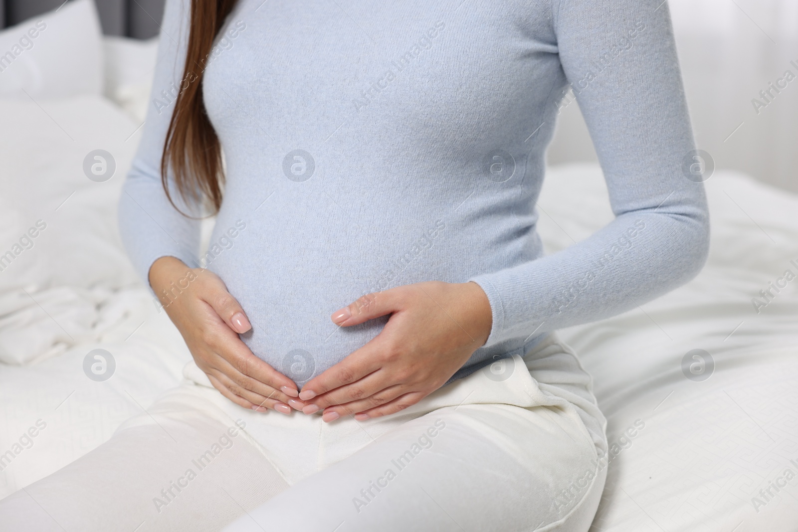 Photo of Pregnant woman on white bed, closeup view