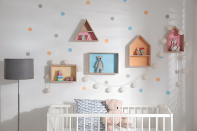 Photo of Cute children's room with house shaped shelves and crib. Interior design