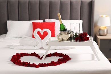 Honeymoon. Swans made with towels, heart of beautiful rose petals and sparkling wine on bed in room