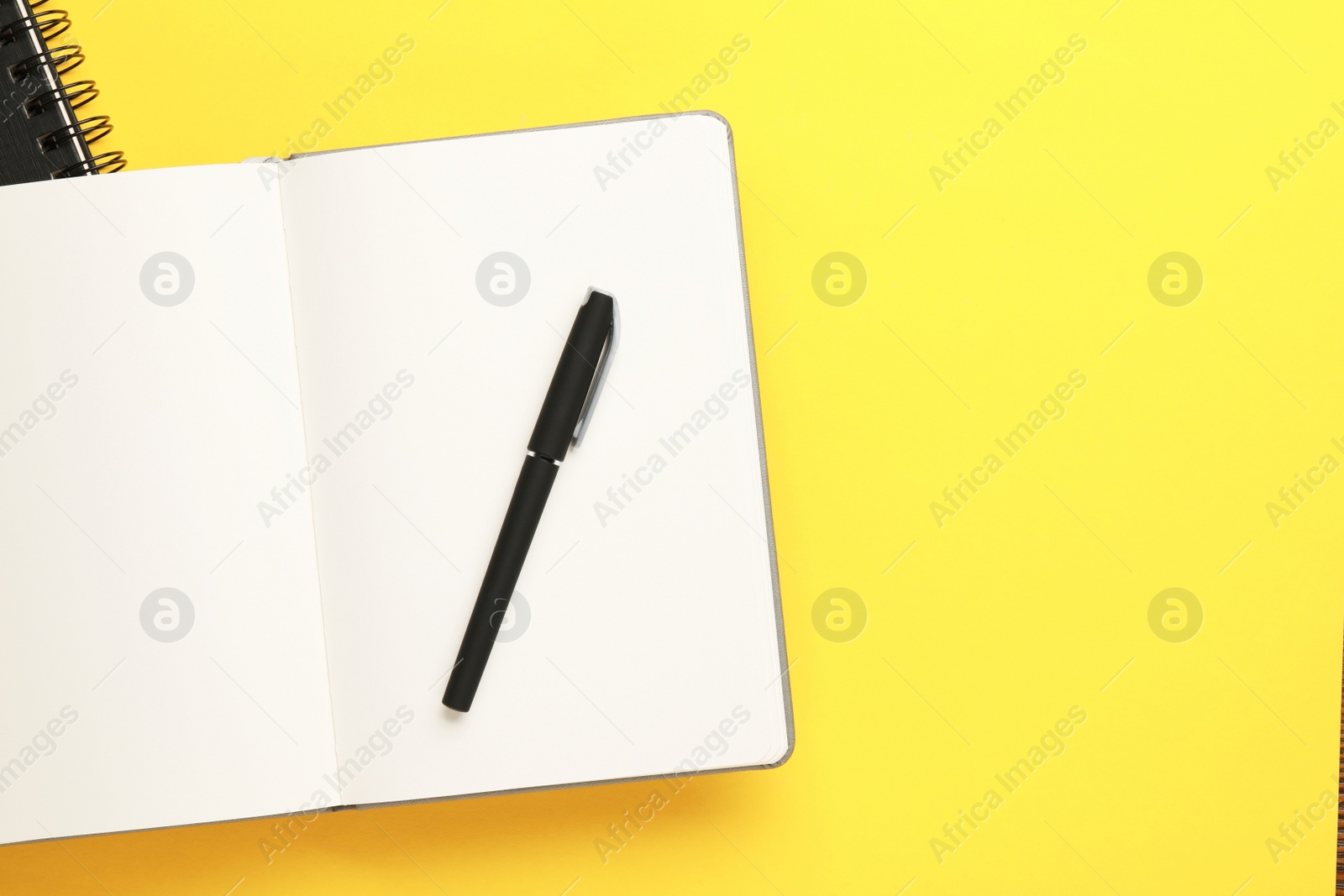 Photo of Notebooks and pen on yellow background, top view. Space for text