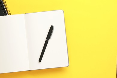 Notebooks and pen on yellow background, top view. Space for text