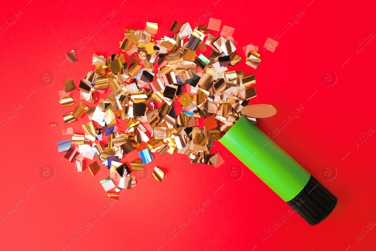 Photo of Shiny colorful confetti bursting out of party popper on red background, flat lay