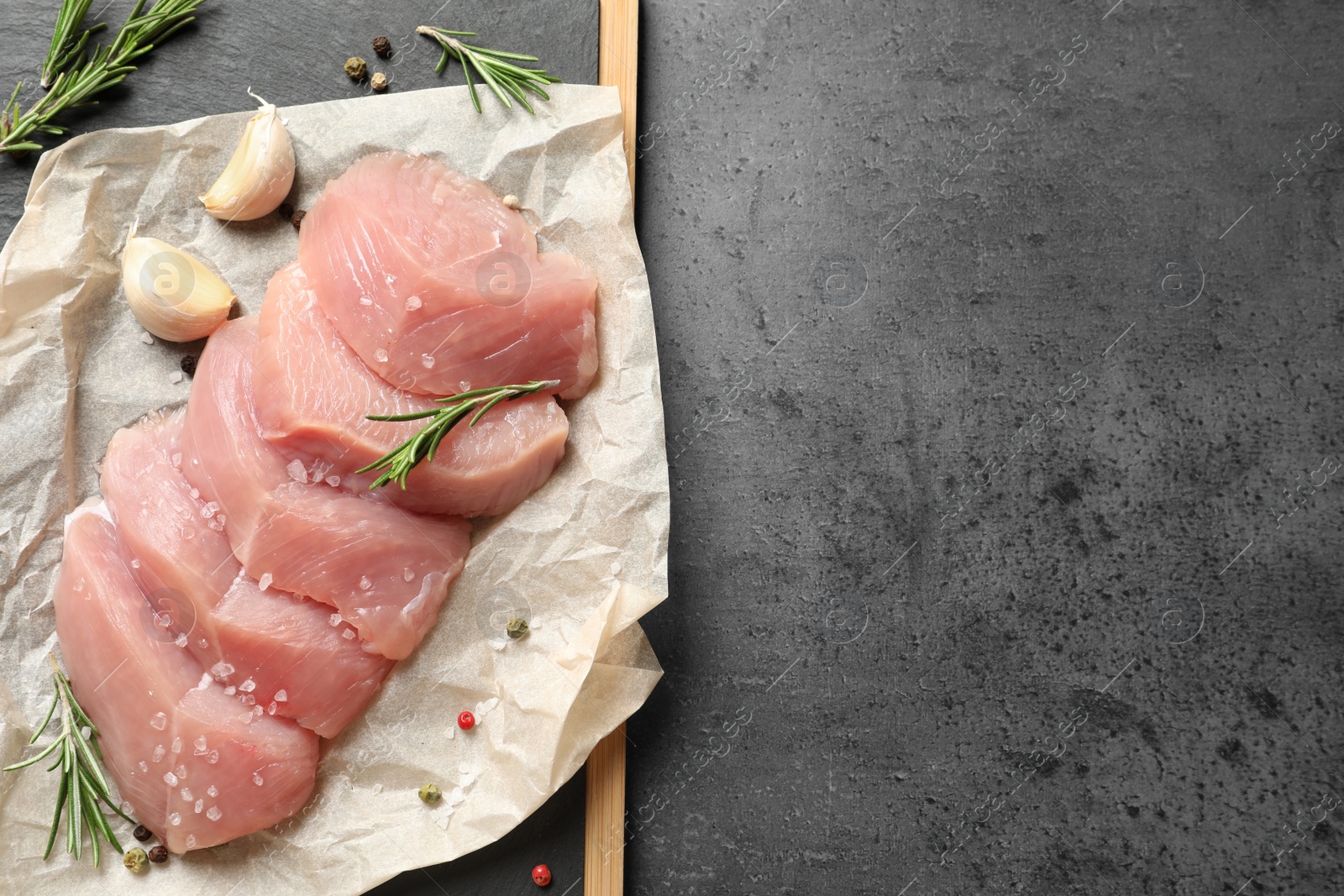 Photo of Board with cut raw turkey fillet and ingredients on grey background, top view. Space for text