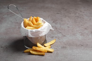 Frying basket with tasty french fries on light grey table, space for text