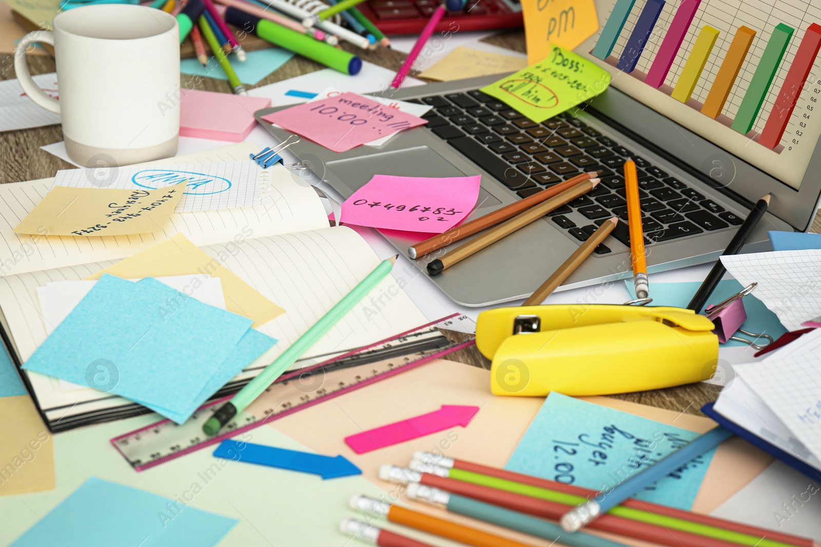 Photo of Laptop, notes and office stationery in mess on desk. Overwhelmed with work