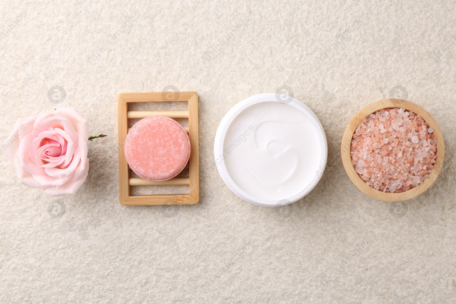 Photo of Flat lay composition with moisturizing cream in open jar and other body care products on light textured table