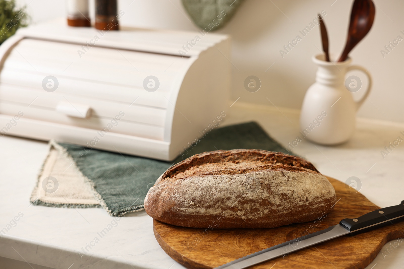 Photo of Wooden bread basket and freshly baked loaf on white marble table in kitchen