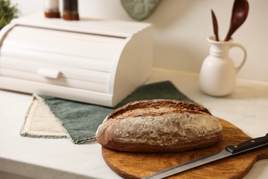 Wooden bread basket and freshly baked loaf on white marble table in kitchen