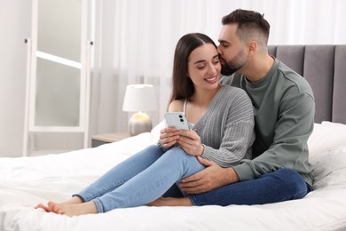 Photo of Happy young couple with smartphone in bedroom. Space for text