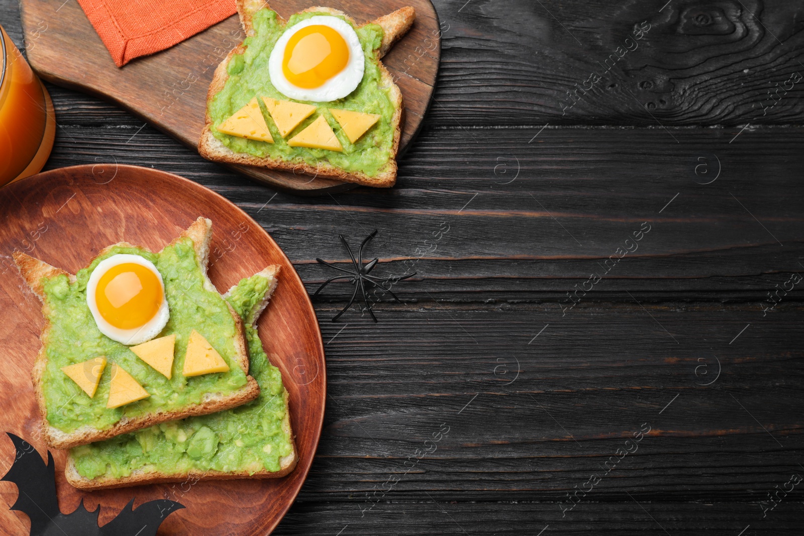 Photo of Halloween themed breakfast served on black wooden table, flat lay and space for text. Tasty sandwiches with fried eggs