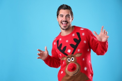 Photo of Portrait of happy young man in Christmas sweater on light blue background