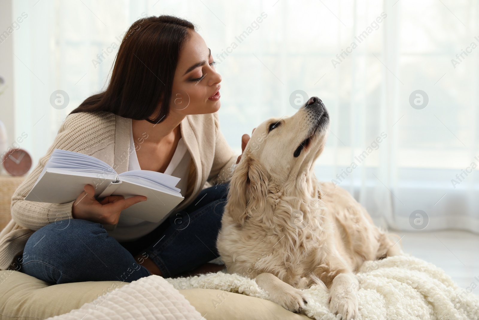 Photo of Young woman with book and her Golden Retriever at home. Adorable pet