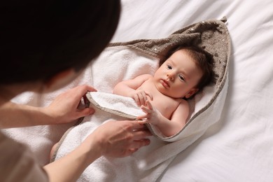 Mother wrapping her cute little baby with hooded towel after bathing on bed, above view