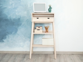 Photo of High wooden table with laptop as stand up workplace near color wall