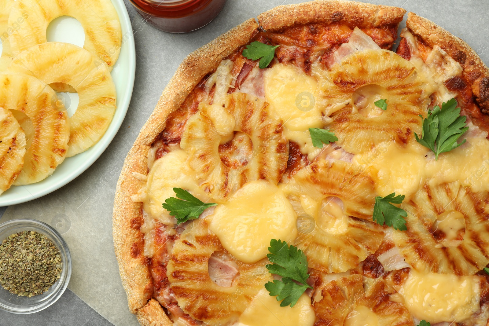 Photo of Delicious pineapple pizza and ingredients on gray table, flat lay