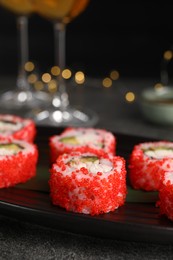 Delicious sushi rolls with tobiko on black plate, closeup