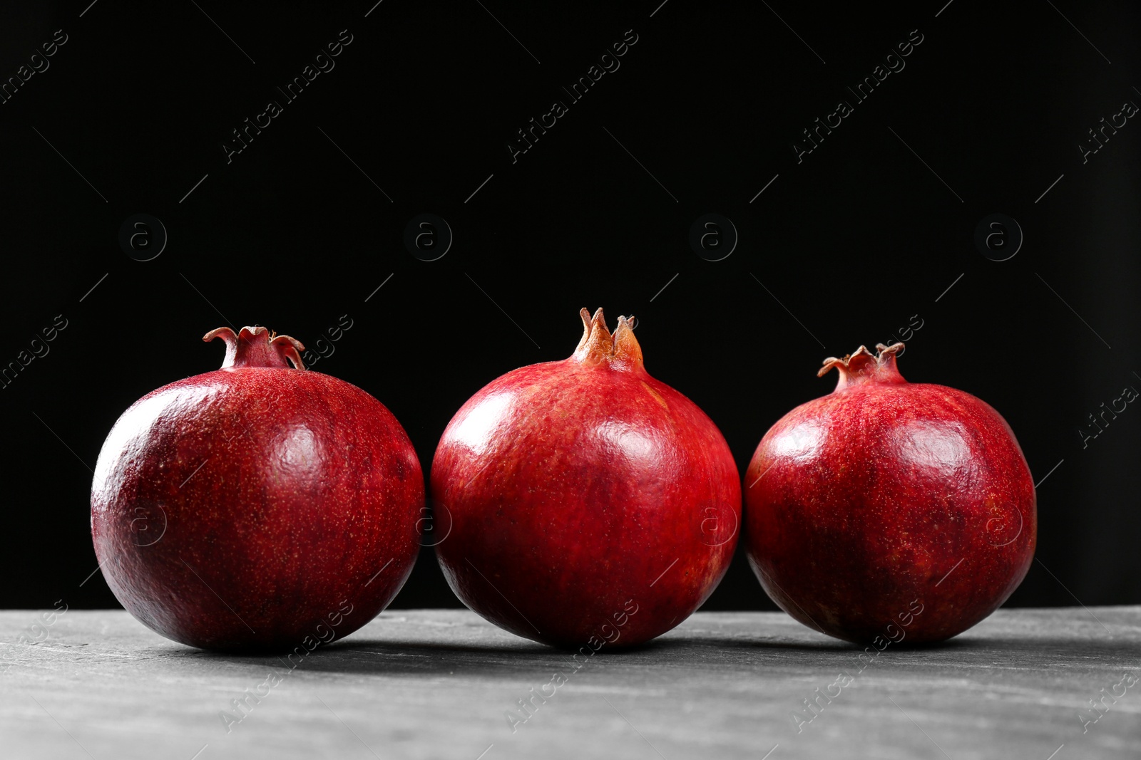 Photo of Ripe pomegranates on table against black background, space for text