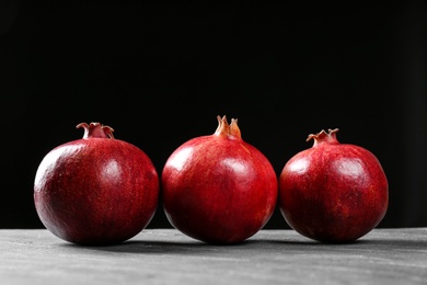 Photo of Ripe pomegranates on table against black background, space for text