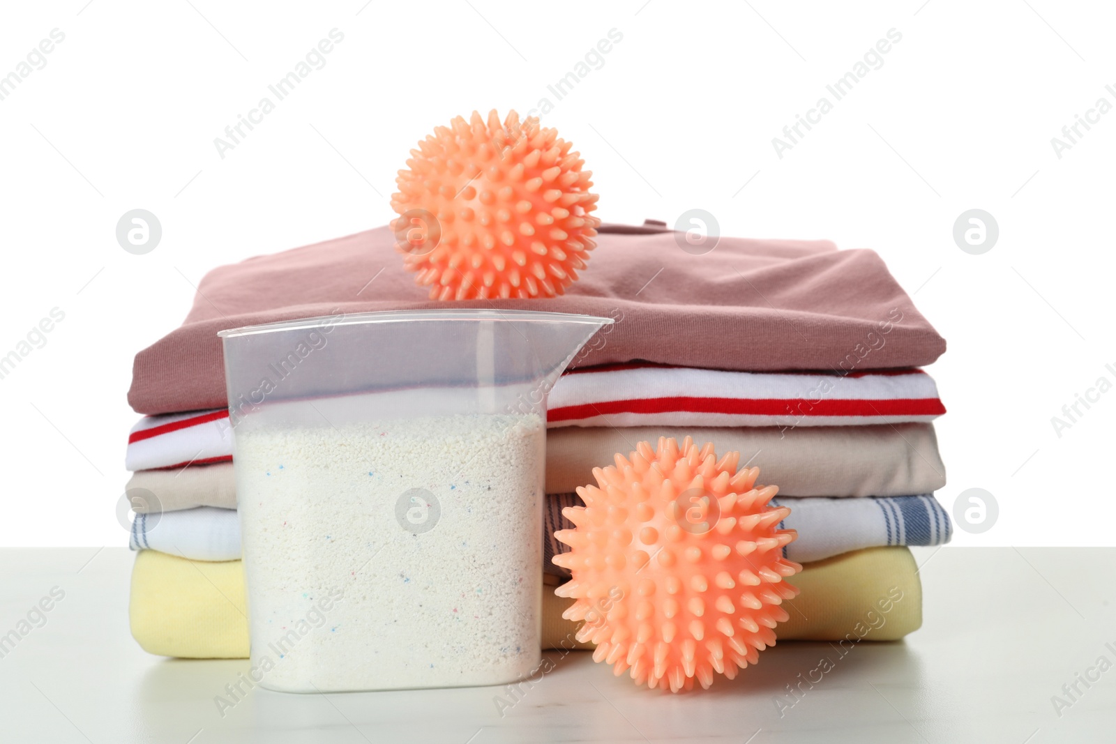 Photo of Orange dryer balls, detergent and stacked clean clothes on marble table against white background
